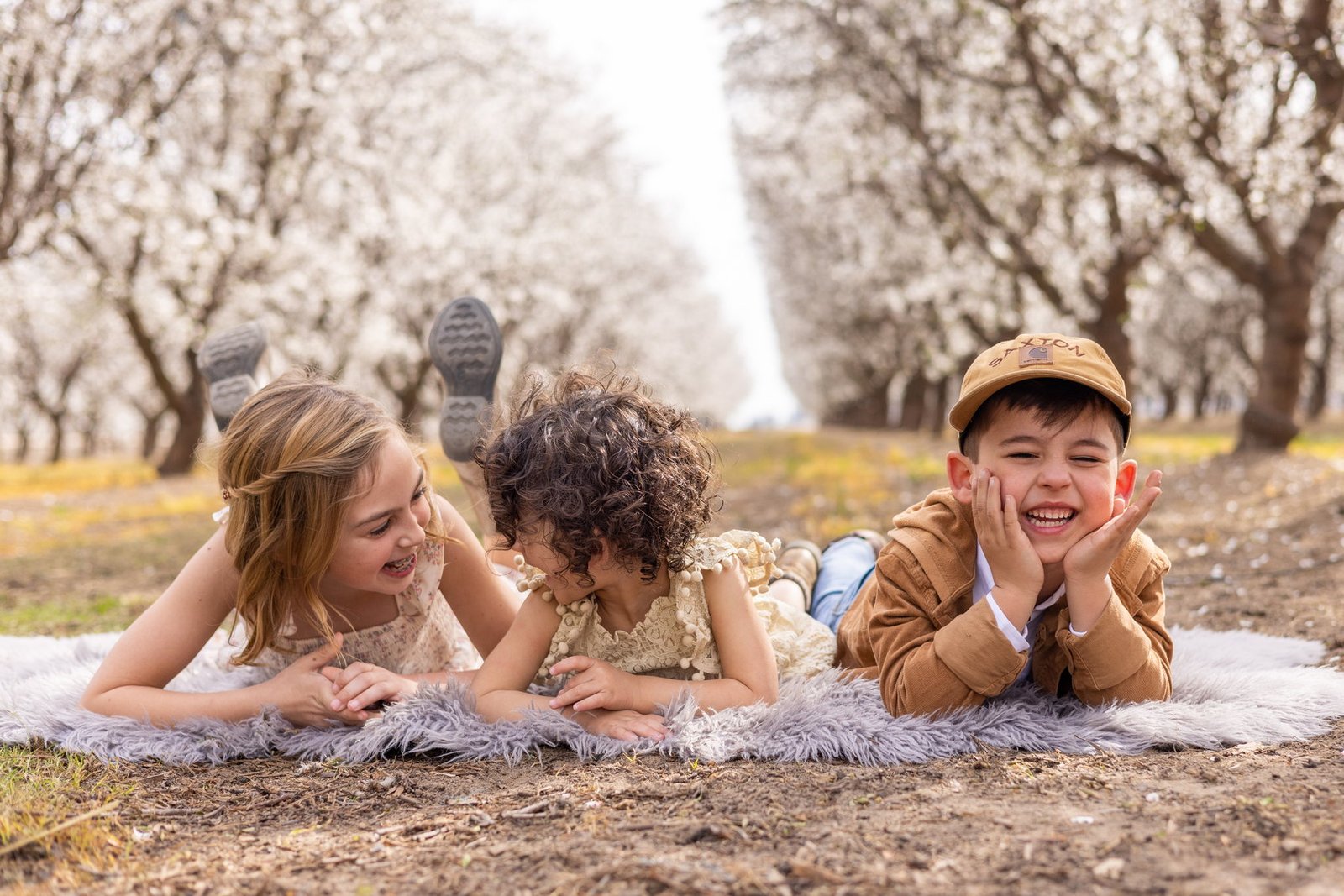 Three children on a blanket in a blossoming orchard